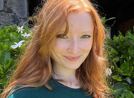 Elaina Tenter, with long red hair and green top in front of green leaves