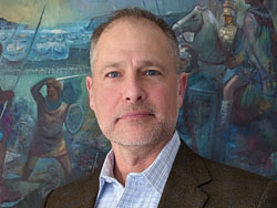 Sean Dudley, in a sport coat, in front of multicolored painting