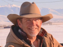 Todd Connor, in tan cowboy hat and tan hooded work jacket, with snowy fields and mountains behind